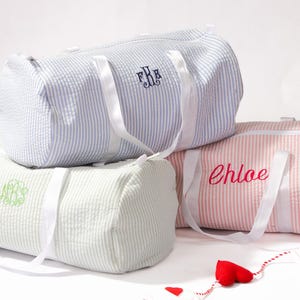 Puede incluir: Tres bolsas de lona rayadas con correas blancas. Las bolsas est&aacute;n personalizadas con los nombres "Chloe", "F.B." y un monograma.