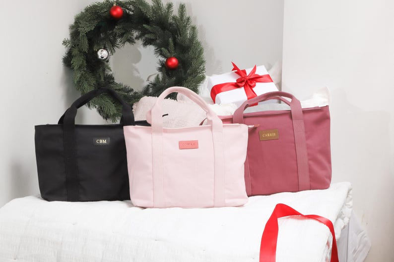 May include: Three tote bags in different colors: black, pink, and burgundy. Each bag has a simple design with two handles and a small label on the front.
