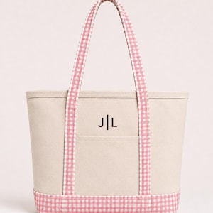 May include: A beige canvas tote bag featuring pink and white gingham patterned handles and a matching gingham base. The front of the bag includes an open pocket and is embroidered with the dark brown monogram letters J|L centered above the pocket.