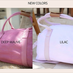 K&ouml;nnte beinhalten: Zwei Canvas-Sporttaschen, eine in tiefem Mauve und eine in Lila. Beide Taschen haben einen braunen Ledergriff und wei&szlig;e Riemen.