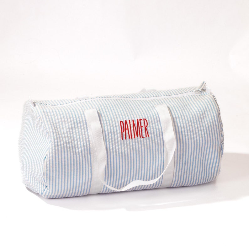 Puede incluir: Una bolsa de lona a rayas azules y blancas con asas blancas y el nombre "PALMER" bordado en rojo.