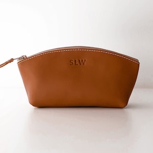 May include: A brown leather zippered pouch with the initials "SLW" embossed on the front.