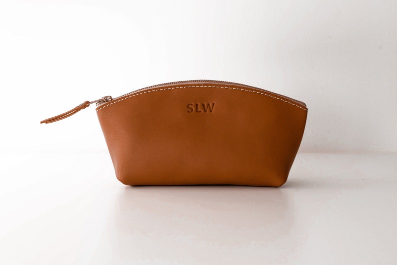 May include: A brown leather zippered pouch with the initials "SLW" embossed on the front.