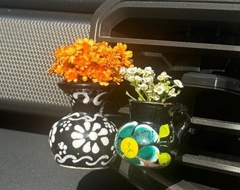 May include: Two small, hand-painted ceramic vases with flowers. The vases are black with white and green floral designs. The flowers are orange and white.