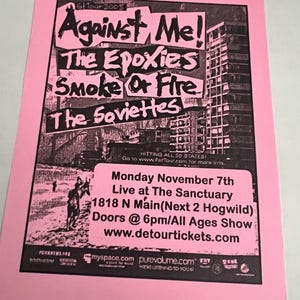 May include: A pink rectangular concert flyer for the 2005 Fat Tour featuring the bands Against Me!, The Epoxies, Smoke Or Fire, and The Soviettes. The black and white graphic includes a city building, text details for the show at The Sanctuary.