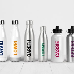 K&ouml;nnte beinhalten: Sechs Edelstahl-Wasserflaschen mit personalisierten Namen. Die Flaschen sind in verschiedenen Farben, darunter Wei&szlig;, Silber und Schwarz. Die Namen auf den Flaschen sind David, Lowri, Gareth, Tommy, Cassie und Bethan.