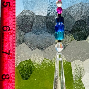 May include: A decorative crystal suncatcher with a clear, faceted teardrop pendant and a string of colorful beads. The beads include clear, pink, and blue hues. The suncatcher is approximately 8 inches long.