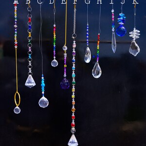 May include: A selection of crystal suncatchers, each with a distinct design. They feature diverse shapes, such as spheres, teardrops, and faceted crystals, strung with colourful beads and chains. The suncatchers are designed to hang and reflect light.