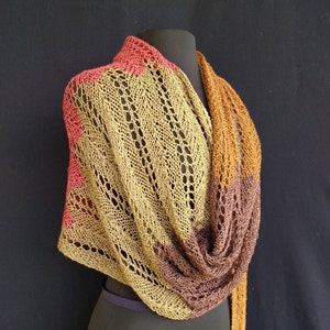 May include: A knitted shawl in shades of brown, orange, and pink. The shawl is draped over a black mannequin.