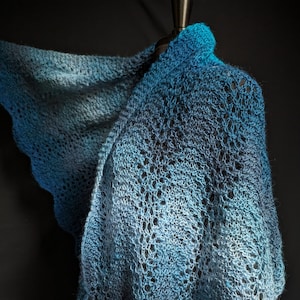 May include: A blue and gray knitted shawl with a lacy pattern. The shawl is draped over a mannequin.