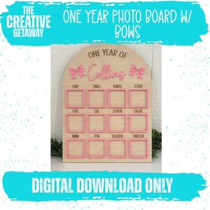 May include: A wooden photo board with pink accents and the text "ONE YEAR PHOTO BOARD W/ BOWS." The board has spaces for twelve photos, with the words "ONE" through "TWELVE" below each frame. The text "ONE YEAR OF" and a name are at the top.