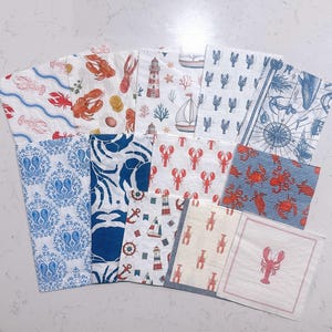 May include: A collection of twelve square paper napkins featuring various nautical and marine-themed patterns. Designs include red lobsters, blue crabs, lighthouses, sailboats, anchors, compasses, and seahorses on white, cream, and striped backgrounds.