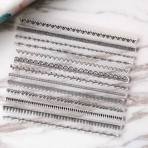 May include: Clear stamp set featuring various black line border designs. The stamps include dotted lines, floral patterns, and geometric shapes. Ideal for scrapbooking, card making, and other paper crafts.