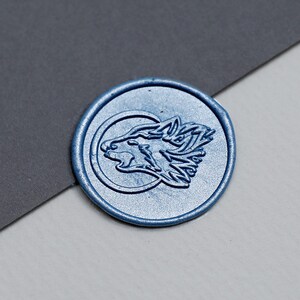 Pode incluir: Um selo de cera azul com um design de cabeça de lobo. O lobo está virado para a esquerda e tem um design detalhado.