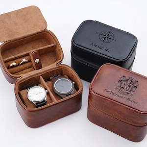 May include: A collection of leather watch and jewelry cases in brown and black. One case is open, displaying rings and two watches. The black case has a compass design and the name "Alexander". The brown case is embossed with "The Harrison Collection".