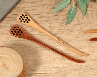 Puede incluir: Dos cucharas de miel de madera, una clara y otra oscura, con cabezas con forma de panal. La cuchara más clara tiene grabado "Unmatched Flavor" en el mango. Las cucharas están sobre una superficie de madera.