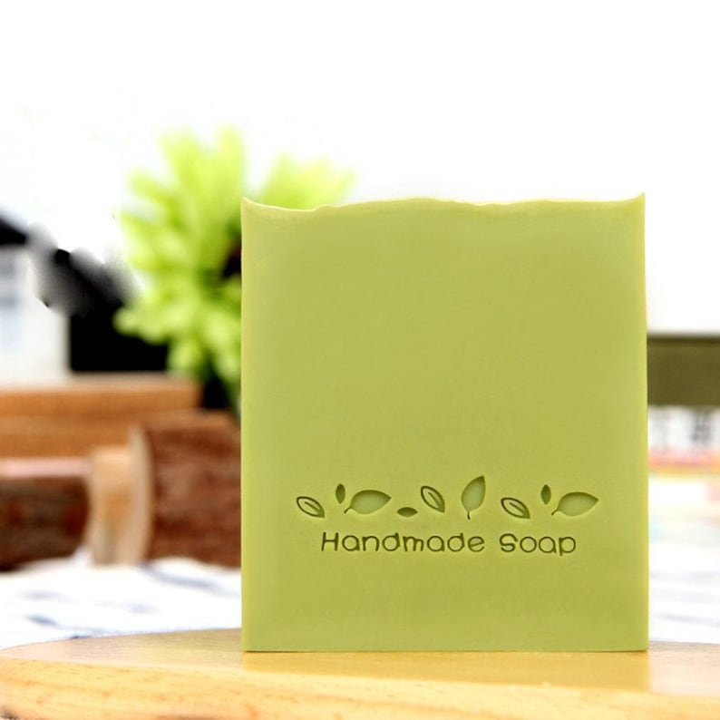 Pu&ograve; includere: Una saponetta verde chiaro con le parole "Handmade Soap" e una fila di motivi a foglia in rilievo sul davanti.