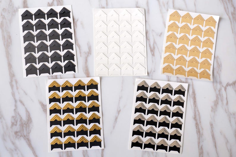 May include: Five sheets of corner stickers for scrapbooking or photo albums. The sheets are white, black, gold, and two shades of brown. Each sheet has 48 corner stickers.