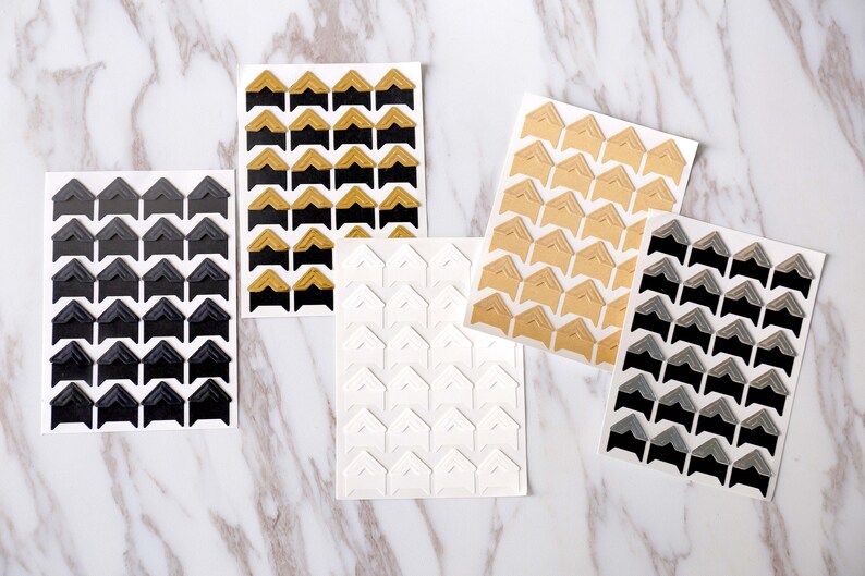 May include: Five sheets of corner stickers for scrapbooking or photo albums. The sheets are white with black, gold, gray, and white corner stickers.