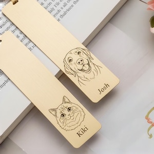 Puede incluir: Dos marcapáginas de madera con retratos de mascotas grabados. Uno presenta un perro con el nombre "Josh", y el otro un gato llamado "Kiki". Ambos marcapáginas tienen un acabado de madera natural y un agujero en la parte superior.