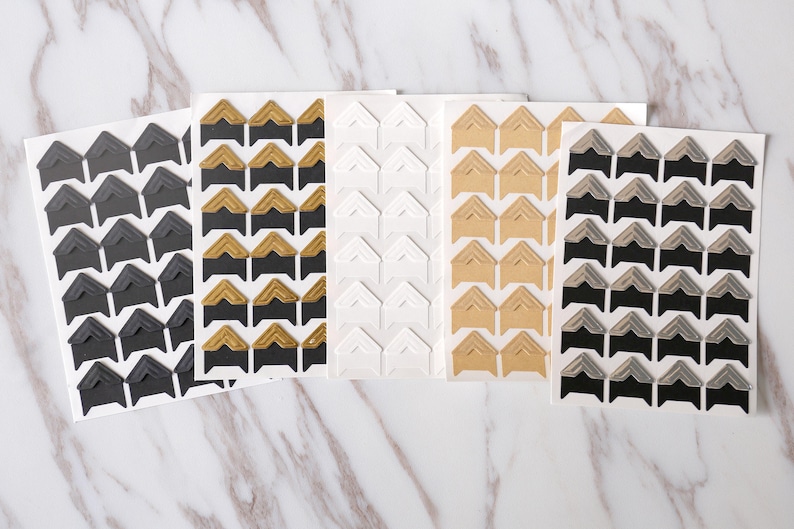 May include: Five sheets of corner stickers for scrapbooking or photo albums. The sheets feature different colors and patterns, including black, gold, white, beige, and silver.