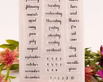 May include: Clear acrylic stamp set featuring months, days of the week, numbers, and symbols. The stamp set includes the words "January" through "December", "Monday" through "Sunday", and numbers 0-9, along with symbols.