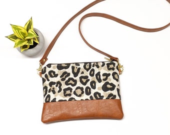May include: A small brown and black leopard print crossbody bag with a brown leather flap and a brown adjustable strap.