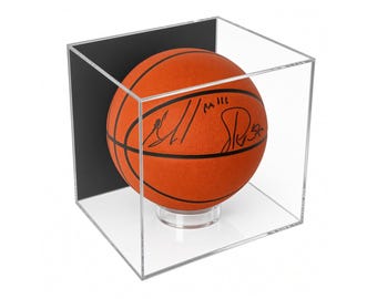 May include: An orange basketball with black seams and black ink signatures displayed inside a clear acrylic cube case. The basketball rests on a small, circular, transparent stand, and the case features a solid black back panel for contrast.