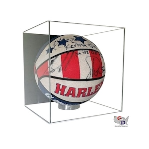 May include: A basketball with red, white, and blue stars and stripes design, signed by multiple players. The basketball is displayed in a clear acrylic cube with a black base.