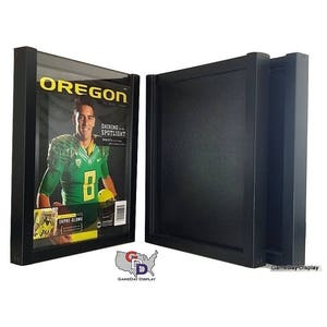 May include: Two black magazine display frames with a magazine featuring a football player in a green and yellow uniform. The magazine cover reads "Oregon" and "Shining in the Spotlight".