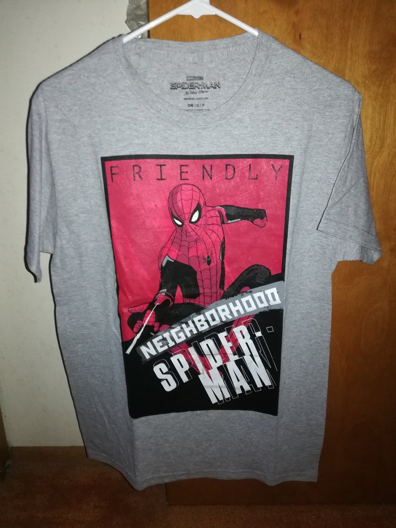 May include: A grey t-shirt with a graphic of Spider-Man in red and black. The shirt displays the words "FRIENDLY NEIGHBORHOOD SPIDER-MAN". The t-shirt is hanging on a white hanger.