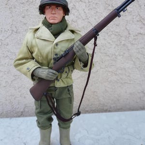 May include: A military action figure dressed in a World War II uniform, including a helmet marked "MP". The figure is holding a brown rifle with a strap. The uniform is olive green and tan, with brown boots.