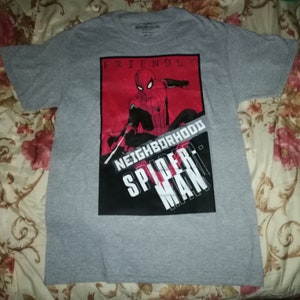 May include: A grey t-shirt with a graphic of Spider-Man in red and black. The words "FRIENDLY NEIGHBORHOOD SPIDER-MAN" are printed on the front. The shirt is made of a soft material and has short sleeves.