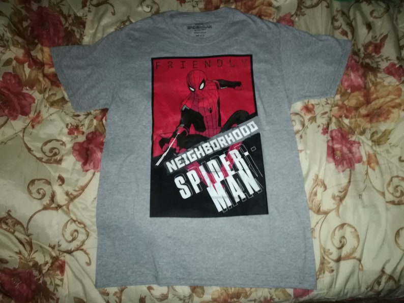 May include: A grey t-shirt with a graphic of Spider-Man in red and black. The words "FRIENDLY NEIGHBORHOOD SPIDER-MAN" are printed on the front. The shirt is made of a soft material and has short sleeves.
