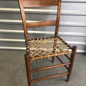 May include: A wooden chair with a woven leather seat. The chair has a simple design with a straight back and four legs.