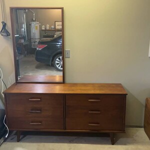 May include: A mid-century modern dresser with six drawers and a mirror above. The dresser is made of dark wood and has a simple design. The mirror is rectangular and has a wooden frame.