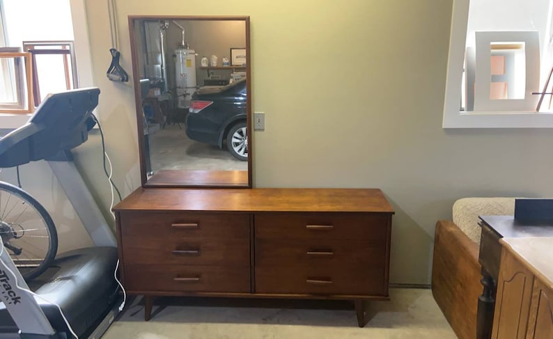 May include: A mid-century modern dresser with six drawers and a mirror above. The dresser is made of dark wood and has a simple design. The mirror is rectangular and has a wooden frame.