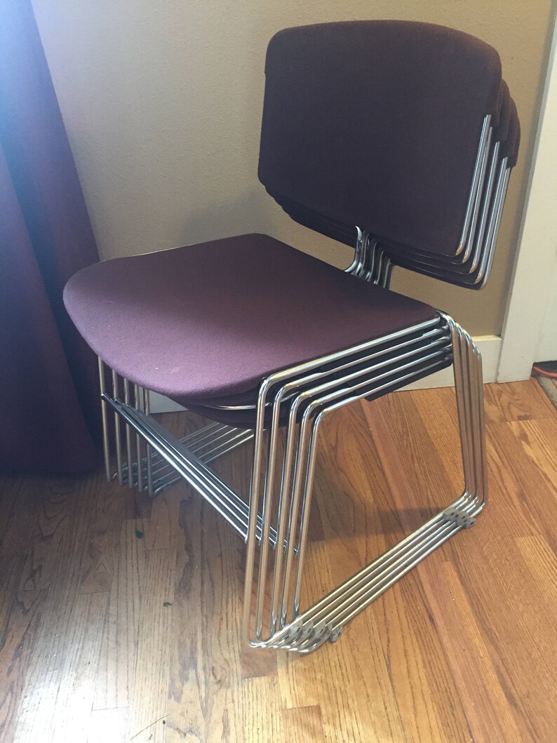 Puede incluir: Una pila de ocho sillas con un marco cromado y asientos de tela color burdeos.