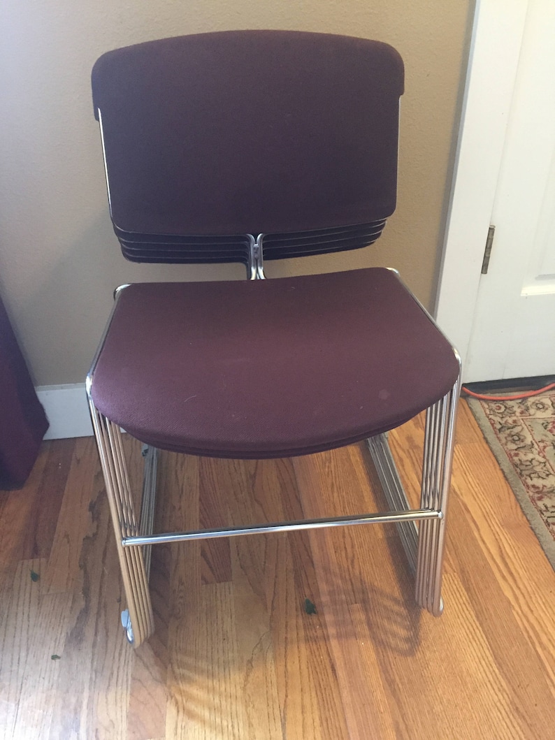 Puede incluir: Una silla apilable con asiento y respaldo de tela color burdeos y estructura cromada.