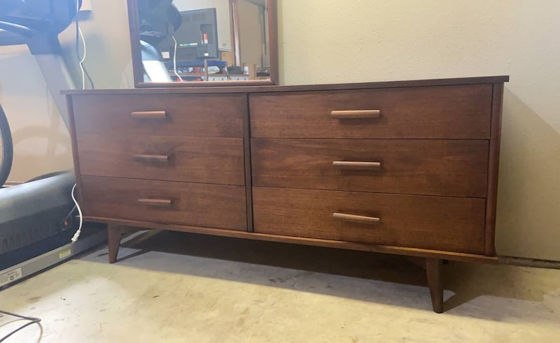 May include: A six-drawer dresser with a dark wood finish and brass hardware. The dresser has a simple, mid-century modern design.