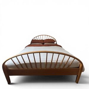 May include: A wooden bed frame with a curved headboard and footboard. The bed is made of light-colored wood and has a mattress with white bedding and brown pillows and a blanket. The bed is set against a white background.
