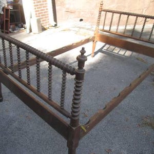 May include: A wooden bed frame with a headboard and footboard made of turned spindles. The frame is made of dark wood and has a simple design.