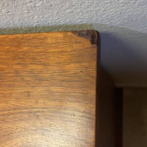 May include: Close-up of the top of a wooden dresser with a light brown finish. The wood grain is visible and there are some scratches on the surface.