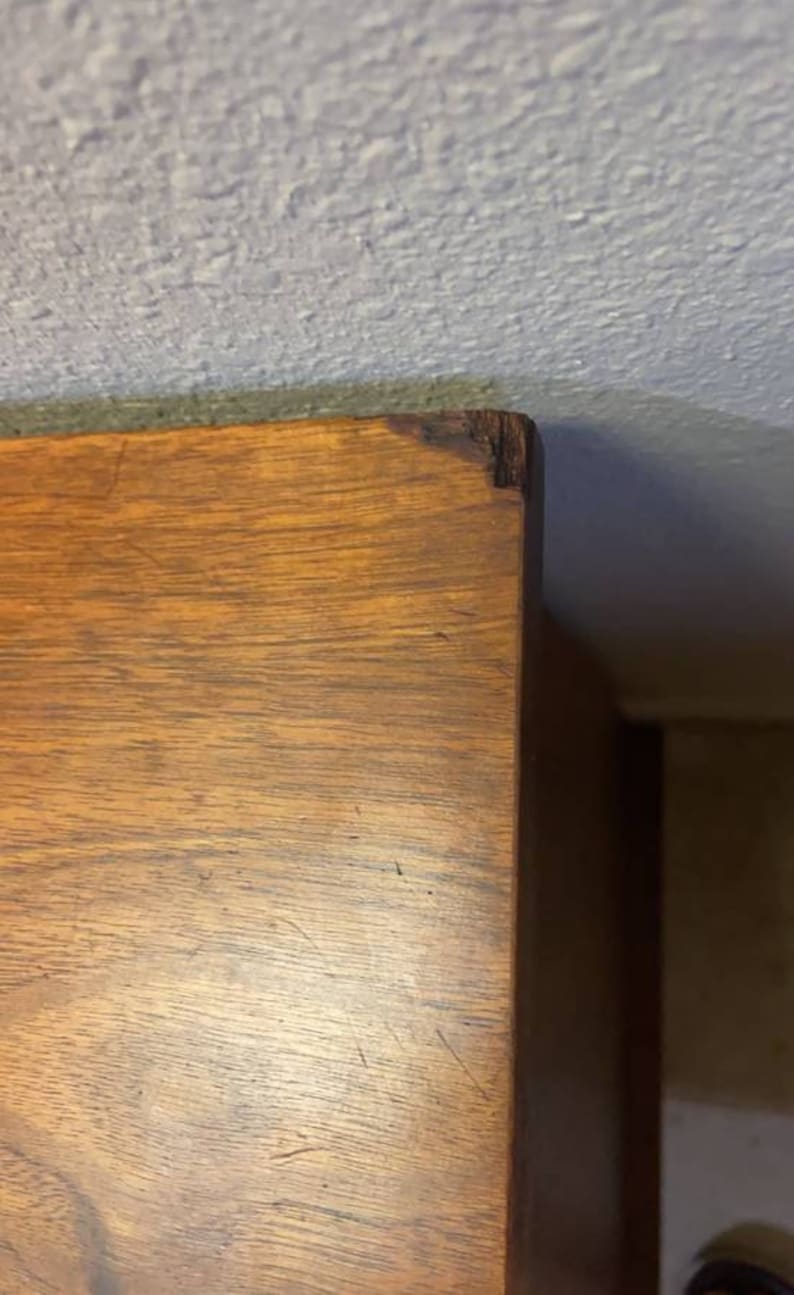 May include: Close-up of the top of a wooden dresser with a light brown finish. The wood grain is visible and there are some scratches on the surface.