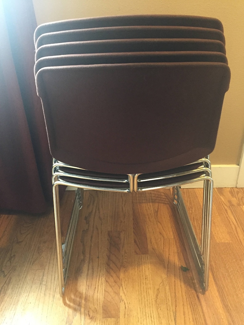 Puede incluir: Una pila de cinco sillas marrones con patas cromadas. Las sillas est&aacute;n apiladas una encima de la otra y est&aacute;n sobre un suelo de madera.