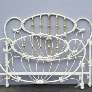 May include: A white metal bed frame with an ornate design. The headboard and footboard feature curved lines, floral accents, and vertical gold-colored bars. The bed frame is a vintage style.