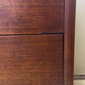 May include: Close-up of a wooden dresser with two drawers. The drawers are made of a rich, dark wood with a smooth finish. The dresser has a simple, classic design.