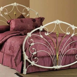 May include: White metal bed frame with ornate scrollwork and a brass finial. The bed is made up with a burgundy bedspread and pillows.