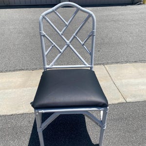 May include: White painted bamboo chair with a black upholstered seat. The chair has a diamond-shaped back.