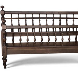 May include: A dark brown wooden bed frame with a spindle headboard and footboard. The bed frame has turned posts and finials, and the headboard features a grid-like design. The bed frame is set against a white background.
